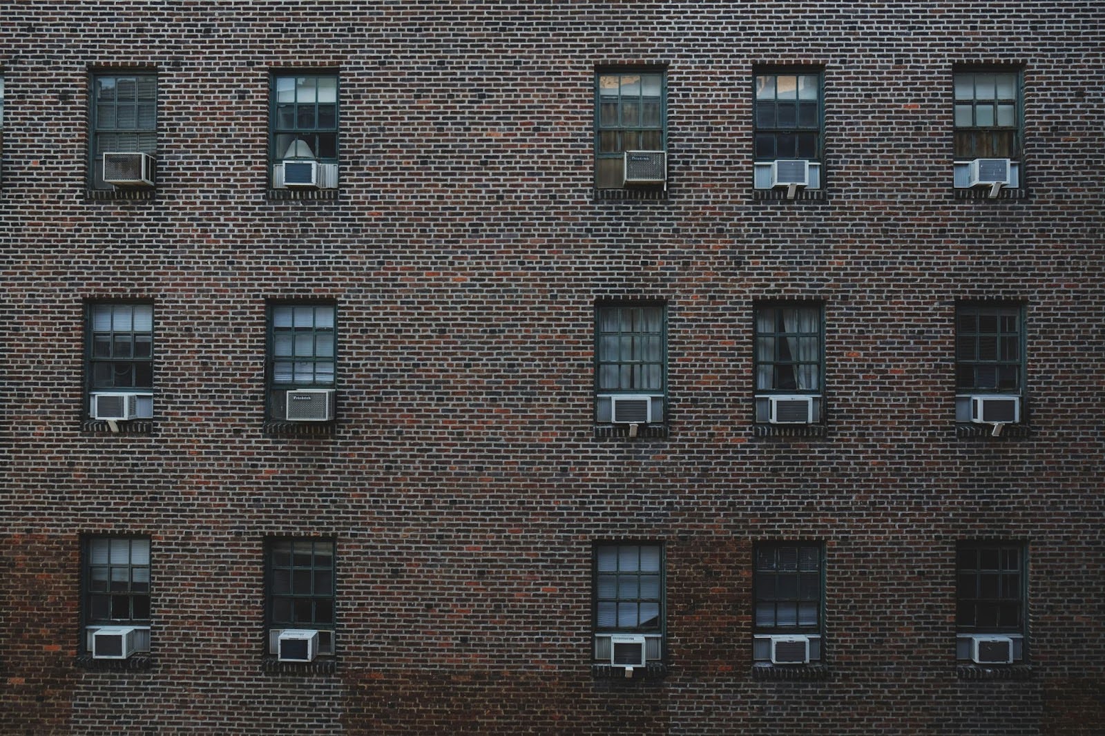 Picture of the side of a red-brick building. There are fifteen windows, each with its own air conditioning unit.