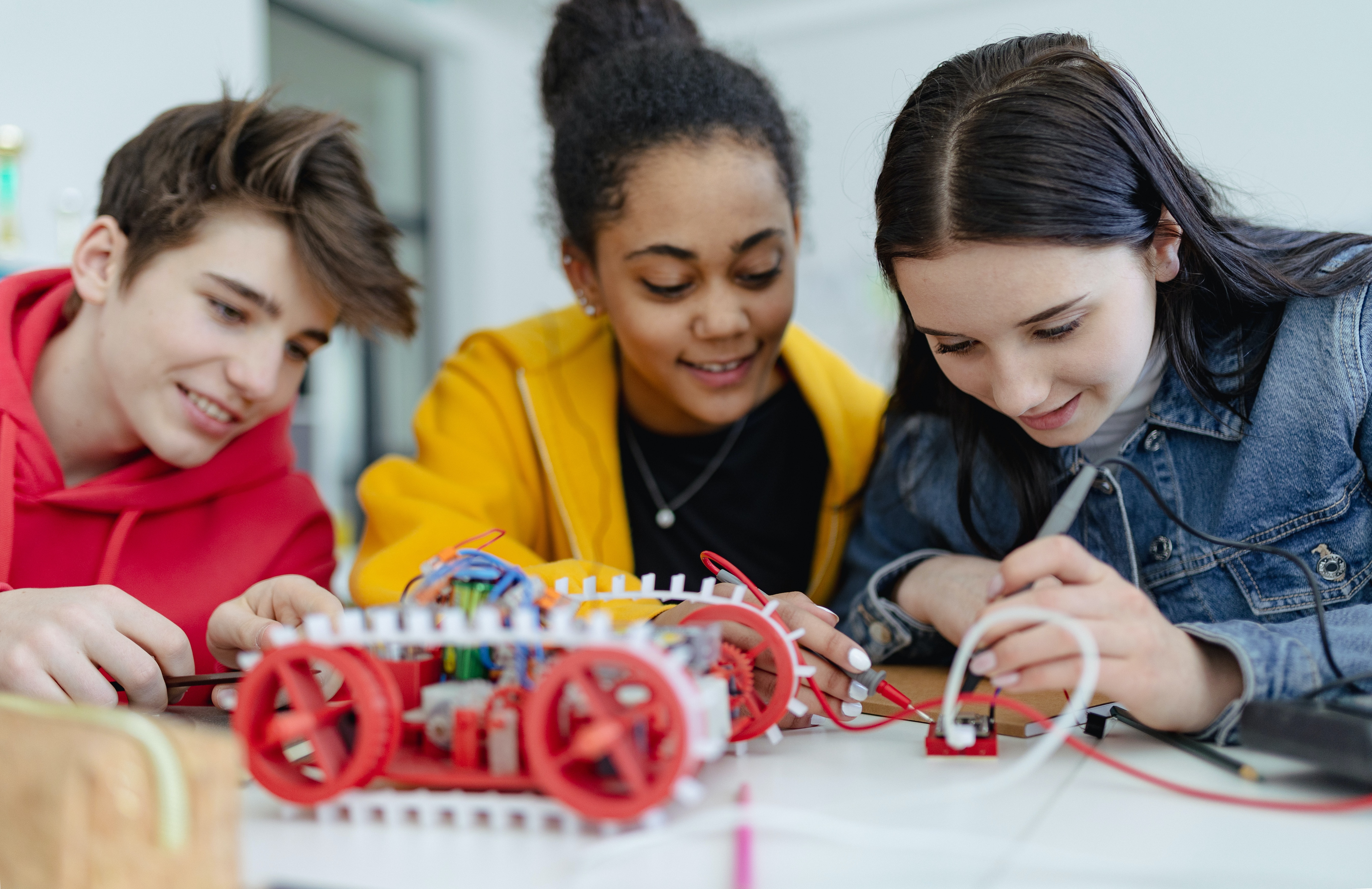 Three students at a desk, working on building a robot.